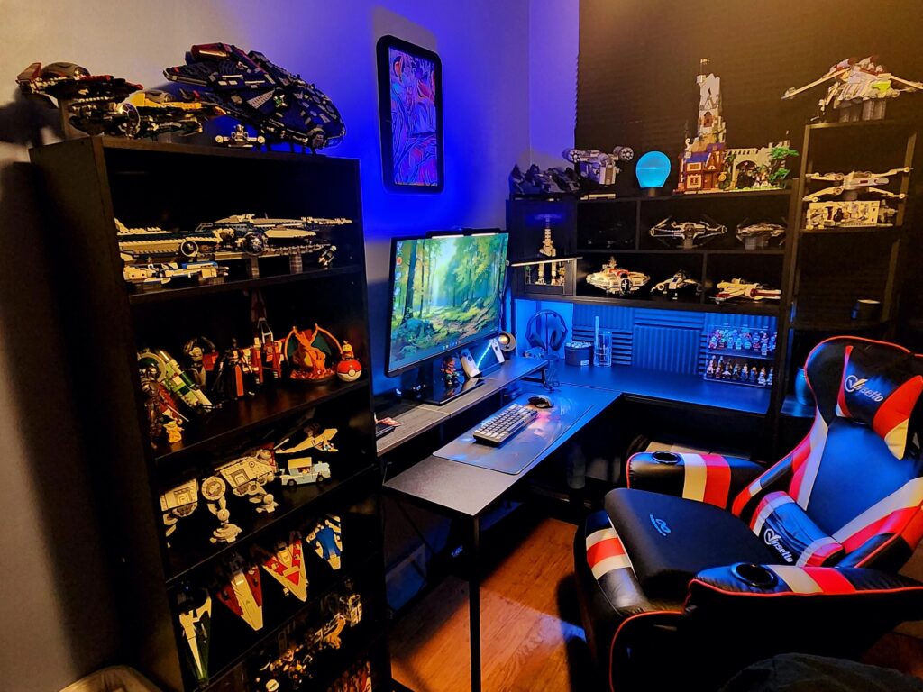 Gaming setup with blue ambient lighting, LEGO spacecraft displays, ultrawide desk, and red-and-black gaming chair.