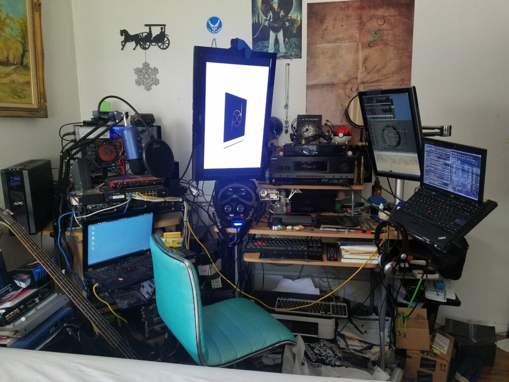 Cluttered multi-monitor computer setup with exposed hardware, laptops, cables, and audio equipment in a crowded room.