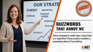 AJnet Magazine title card for "Buzzwords That Annoy Me," featuring a smiling corporate presenter standing in front of a presentation filled with business buzzwords such as "Synergy," "Innovation," and "Thought Leader."