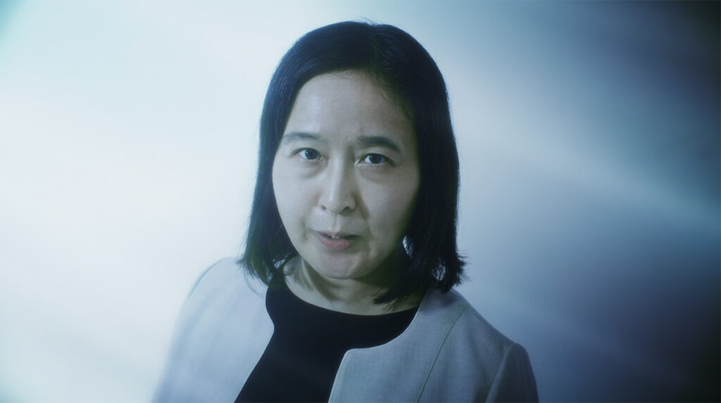 Sister Sumire in a live-action Fire Force scene, staring forward in a dim, blue-tinted setting