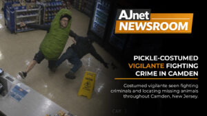 AJnet Newsroom title card showing a blurry security camera image of a pickle-costumed vigilante knocking down a robber in a convenience store.